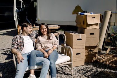 Smiling couple sitting on chair while relocating to new house