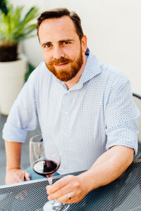 Red haired man with moustache sitting at table with glass of red wine