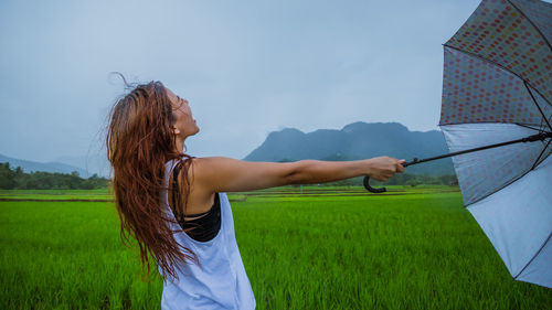 Woman holding umbrella while standing on field against sky