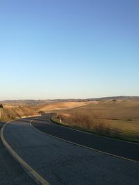 Road passing through landscape against clear blue sky