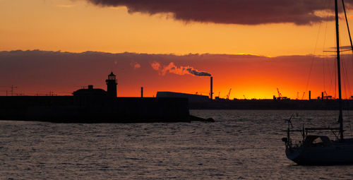 Silhouette sailboats in sea against orange sky