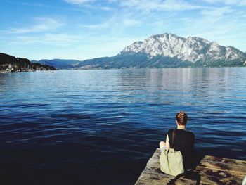 Rear view of woman sitting on pier while looking at lake against sky