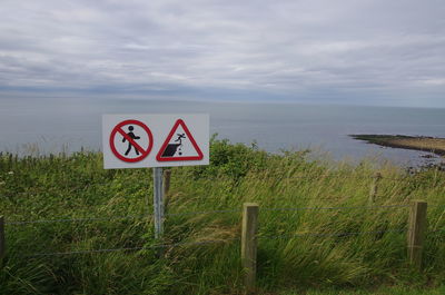 Road sign by sea against sky