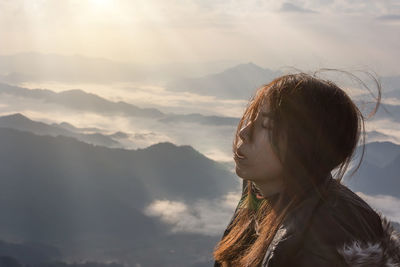Portrait of young woman looking at mountains against sky