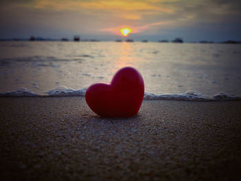 Heart shape on sand at beach against sky during sunset