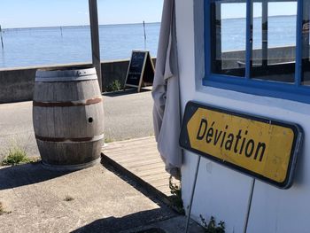 Information sign by sea against sky