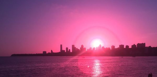 City buildings by sea against sky during sunset