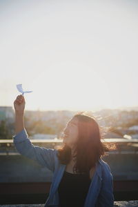 Woman flying paper airplane against sky