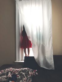 Rear view of girl standing on sofa by window at home