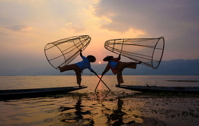 Low angle view of men fishing in sea against sky during sunset