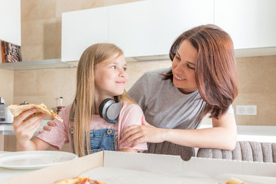 Mother looking at daughter eating pizza at home