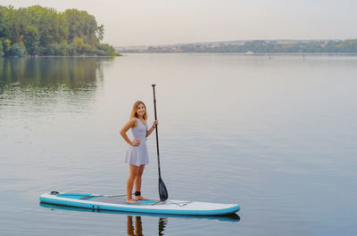 Young woman in a dress swims on the lake on surfboard