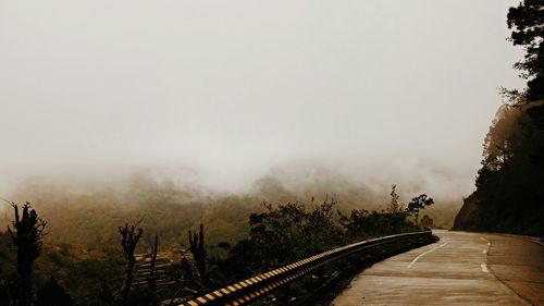 Empty road by mountains against sky during foggy weather
