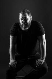 Portrait of young man sitting against black background