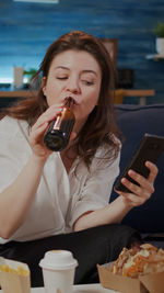 Young woman using mobile phone while sitting on laptop