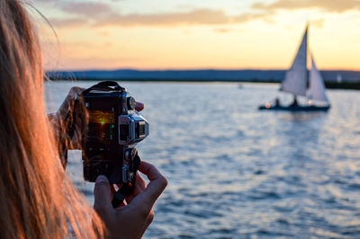 Woman photographing sea against sky during sunset