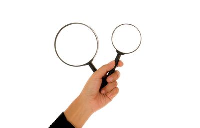 Cropped hand of woman holding magnifying glasses against white background