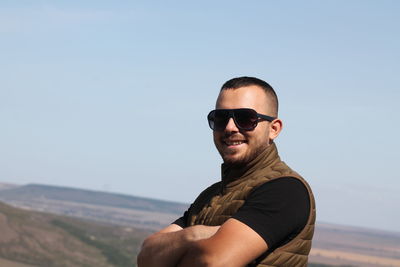 Portrait of young man wearing sunglasses standing against sky