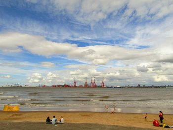 People at beach against sky in city