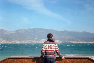 Rear view of man standing by sea against sky