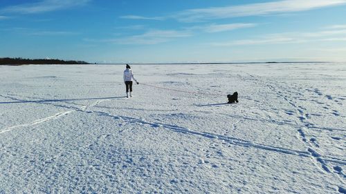 Rear view of woman with dog walking on snow covered landscape against sky