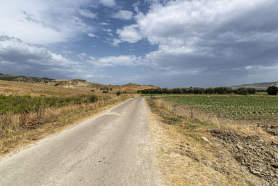 Empty road amidst field against sky