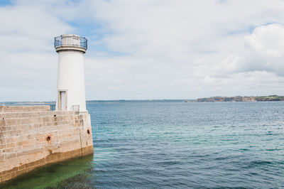 Lighthouse amidst sea and buildings against sky