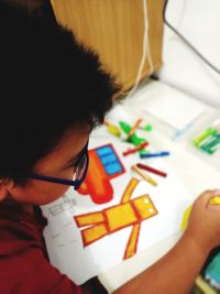 High angle portrait of child holding multi colored art on table