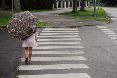 Rear view of girl with umbrella walking on road