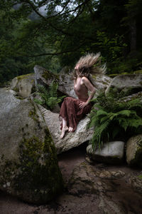 Woman throwing her hair over her had sitting in beautiful landscape on a stone