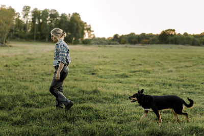 Female farmer with dog walking on field during sunset