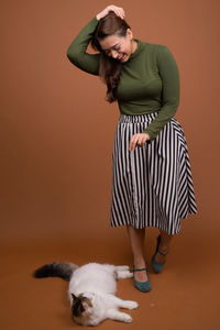 Woman with cat standing against brown background