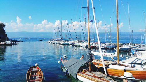 Sailboats moored on harbor against blue sky during sunny day