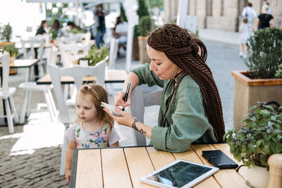 Freelance parents. busy working mom with cell phone and tablet working in street cafe with baby