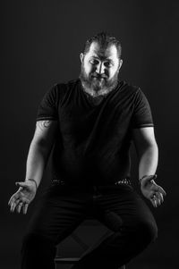 Worried man gesturing while sitting on chair against black background