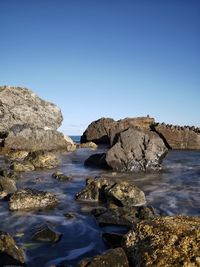 Rocks on beach against clear blue sky