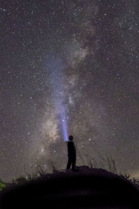 Silhouette man with illuminated flashlight on hill against star field