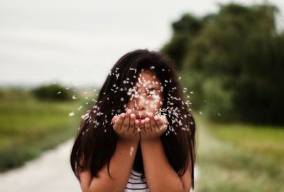 Girl blowing petals while standing against sky in park