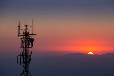 Silhouette of communications tower against orange sky