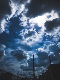 Low angle view of silhouette electricity pylon and buildings against sky