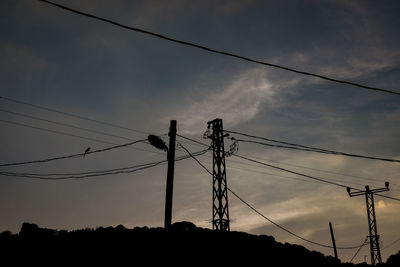 Low angle view of silhouette electricity pylon against sky at sunset