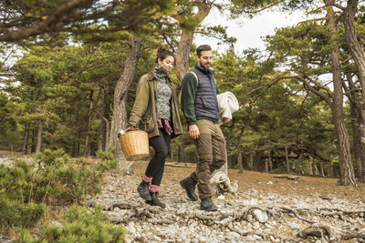 Couple carrying blanket and basket in forest