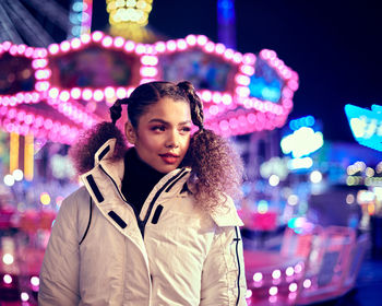 Smiling woman standing against illuminated ferris wheel at night