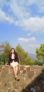 Young woman sitting on rock against sky