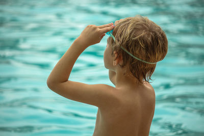Rear view of shirtless boy wearing swimming goggles while standing by sea