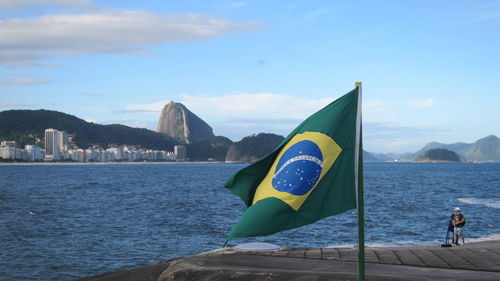 Brazilian flag at sea shore against sky