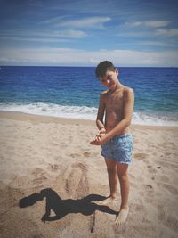 Portrait of shirtless boy standing at beach against sky