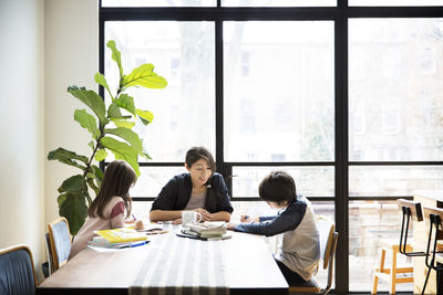 Mother teaching children on table at home on sunny day