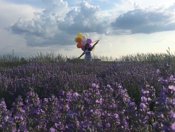 Woman holding balloons while standing on field against sky