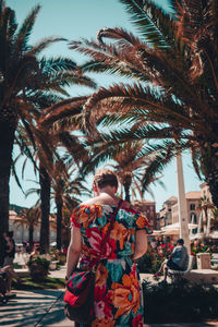 Rear view of woman standing against palm trees